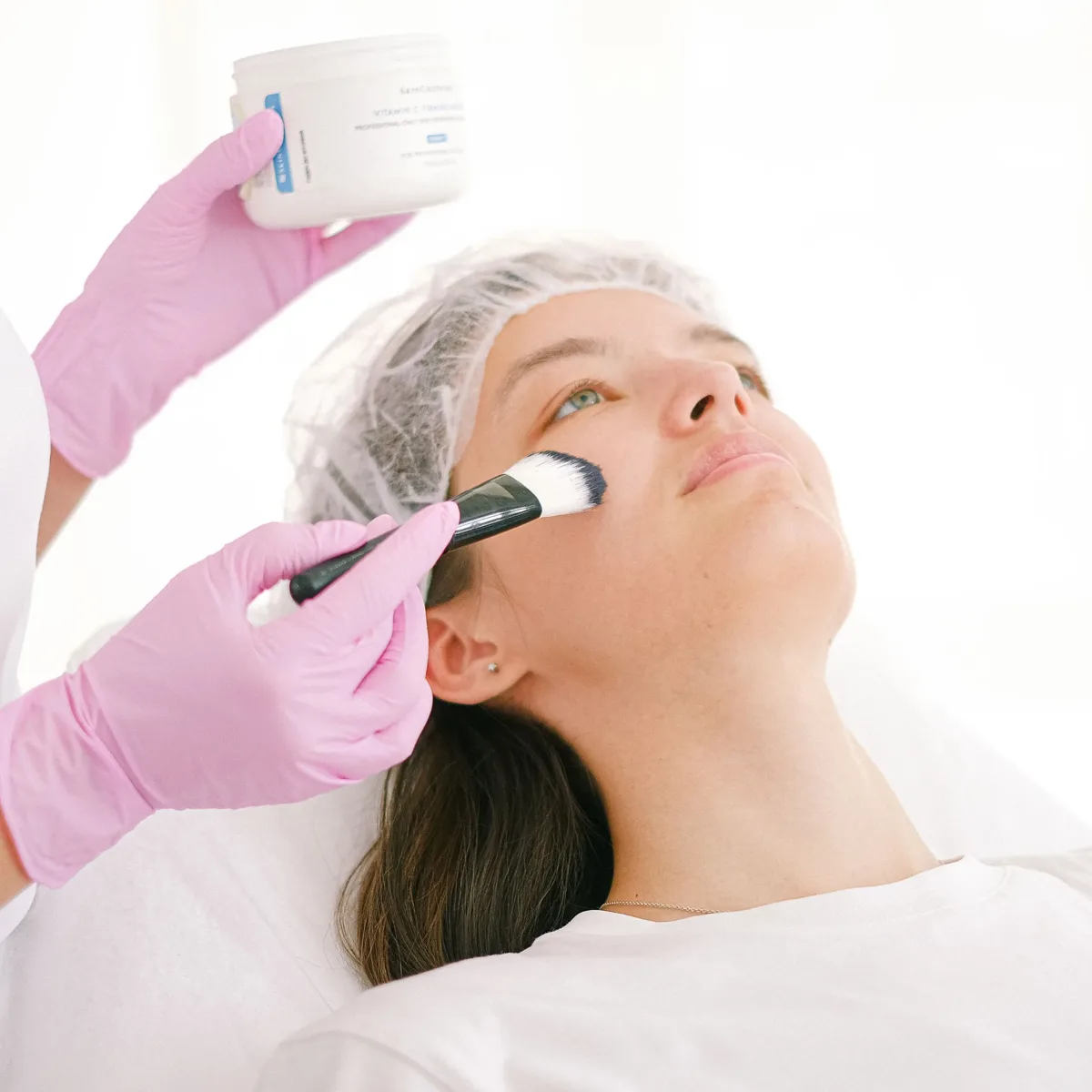 Esthéticienne posant un masque au pinceau sur le visage d’une cliente allongée